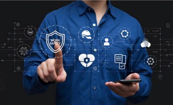 Man pointing to a digital work safety shield icon surrounded by health, hard hat, and compliance icons on a dark background.